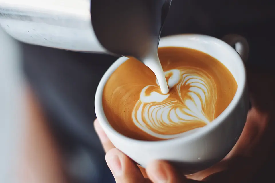 Someone pouring milk into a cup of coffee, while making a decrotive heart shape. Photoby Chevanon Photography
